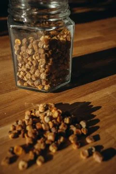 Glass jar of bee bread with granules spilled on a wooden table. Stock Photos
