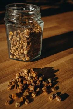 Glass jar of bee bread with granules spilled on a wooden table. Stock Photos