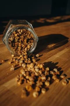 Glass jar of bee bread with granules spilled on a wooden table. Stock Photos
