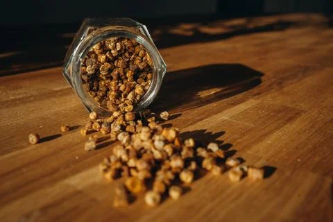 Glass jar of bee bread with granules spilled on a wooden table. Stock Photos