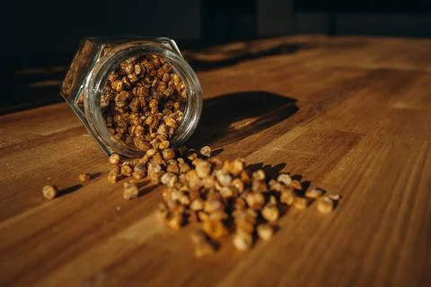 Glass jar of bee bread with granules spilled on a wooden table. Stock Photos