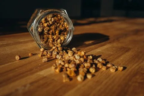 Glass jar of bee bread with granules spilled on a wooden table. Stock Photos