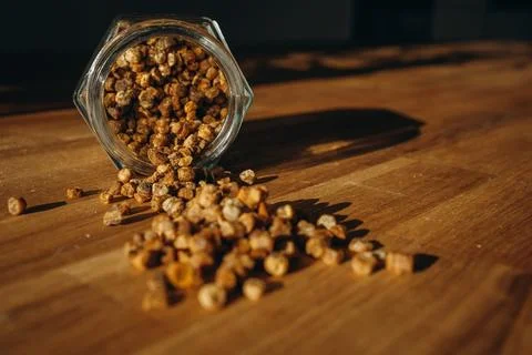 Glass jar of bee bread with granules spilled on a wooden table. Stock Photos