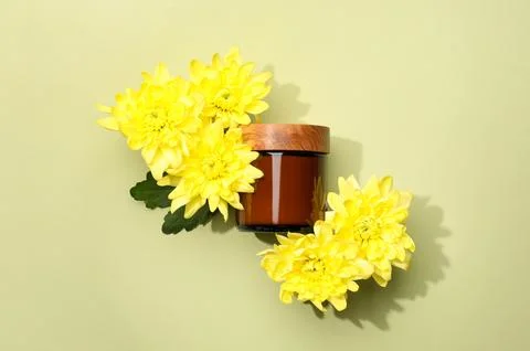 Glass jar of face cream and flowers on pale olive background, flat lay Stock Photos