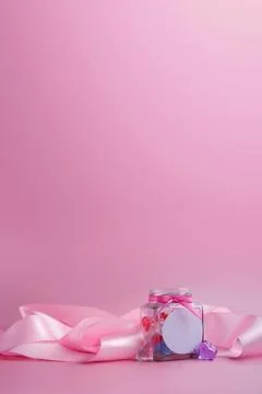 Glass jar with multicolored hearts and pink silk ribbon on a pink background. Stock Photos
