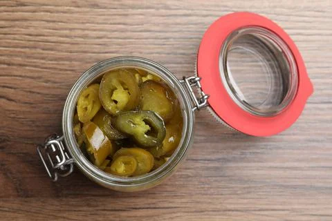 Glass jar with slices of pickled green jalapeno peppers on wooden table, top  Stock Photos