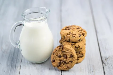 Glass jug with milk and chocolate chip cookies on a wooden background Stock Photos