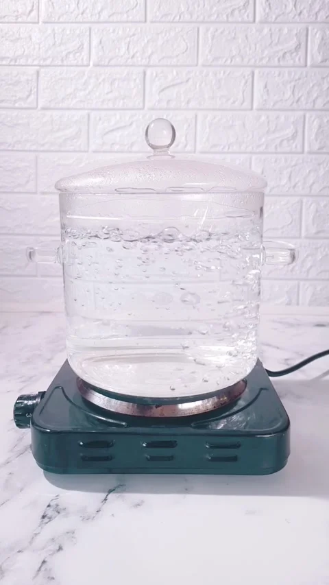 A glass kettle sits on a heating element in a kitchen. Water inside the kettle Video stock 347332228