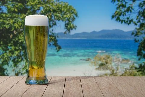 Glass of light beer on table with view of beautiful beach and sea with turq.. Stock Photos