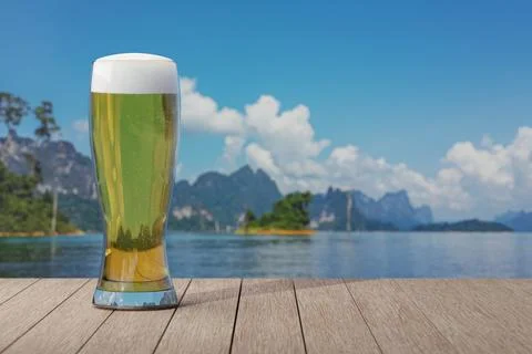 Glass of light beer on table with view of lake with islands with mountains .. Foto stock