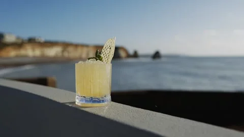 A glass of liquid with a leaf on top is sitting on a ledge overlooking the ocean Stock Footage 295993874