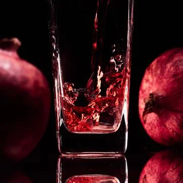 Glass in the low-key lighting with two pomegranates and juice Stock Photos
