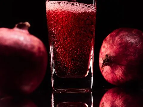 Glass in the low-key lighting with two pomegranates and juice Stock Photos