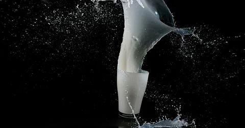 Glass for Milk exploding against Black Background Foto stock