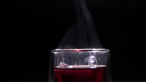 A glass mug with red fruit tea evaporates on a black background Stock Footage 144431323