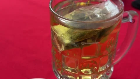 Glass mug of tea with tea bag and lemon slice on red tablecloth cozy homemade Stock Footage 345728577