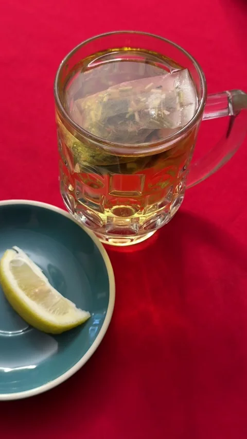 Glass mug of tea with tea bag and lemon slice on red tablecloth cozy homemade Stock Footage 345735306