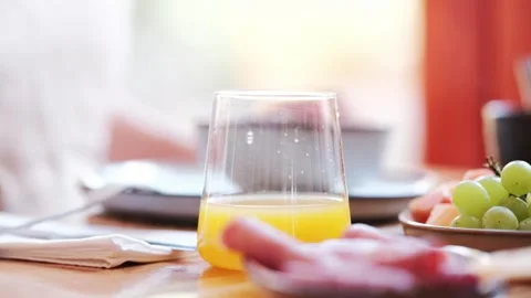 A glass of orange juice on a breakfast table setup as someone eats a fruit bowl Stock Footage 339665854