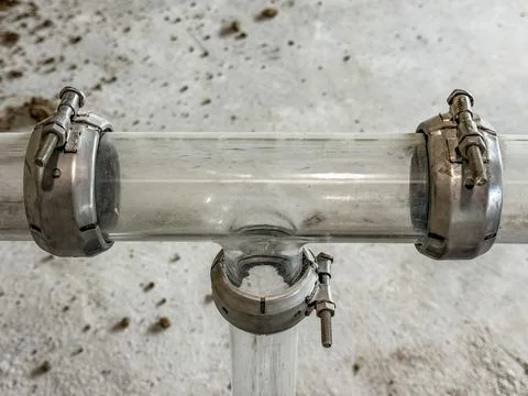 Glass pipe system featuring a tee junction joint secured by metal couplings. Stock Photos