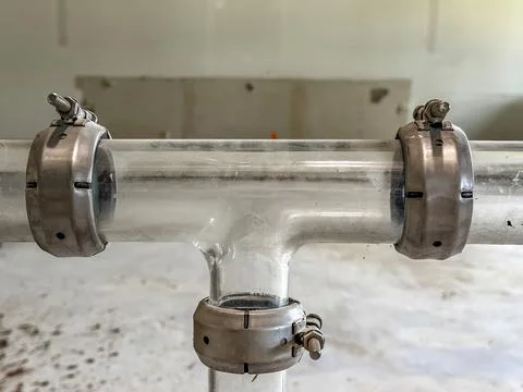 Glass pipe system featuring a tee junction joint secured by metal couplings. Stock Photos