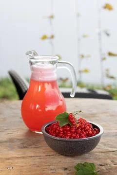 Glass pitcher of pink currant drink beside ceramic bowl of fresh red currants Stock Photos