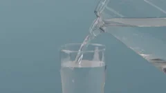 pouring water from pitcher into the glass on light blue background Stock  Photo