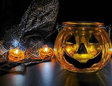 A glass pumpkin jar with pumpkin string lights in the background in a dark s Stock Photos