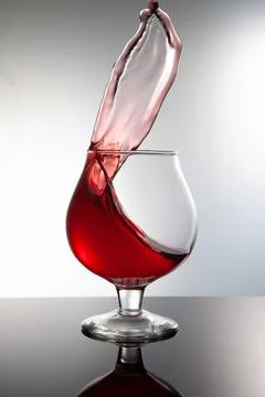 A glass with a red drink explodes with splashes on a gray background Foto stock