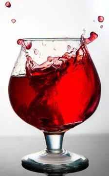 A glass with a red drink explodes with splashes on a gray background Foto stock