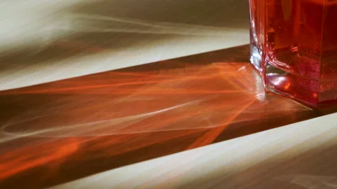 Glass with a red drink through which passing the rays of light on the table. 4K 库存影片 106684330