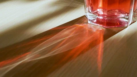 Glass with a red drink through which passing the rays of light on the table. 4K 動画素材 106684405