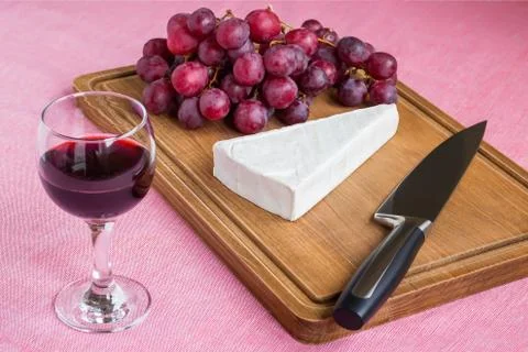 Glass of red wine and a triangular piece of Brie cheese, red sweet grapes Stock Photos