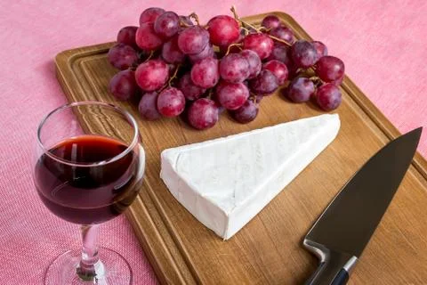 Glass of red wine and a triangular piece of Brie cheese, red sweet grapes Stock Photos