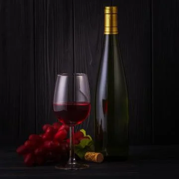 Glass of red wine with a bottle and grapes on back Stock Photos