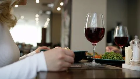 A glass of red wine on a dining table with a woman enjoying a meal in a res.. Fotos Stock