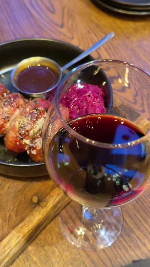 A glass of red wine Serving of the baked thick short sausages with leaf Stock Footage 323921374
