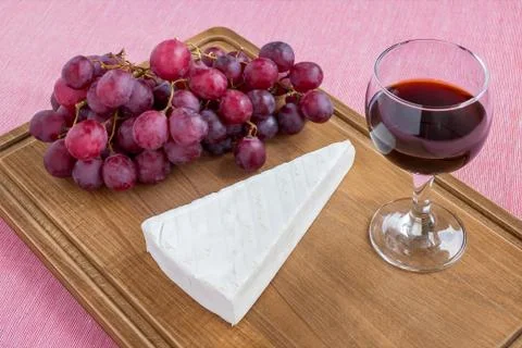 Glass of red wine, triangular piece of Brie cheese and red sweet grapes Stock Photos