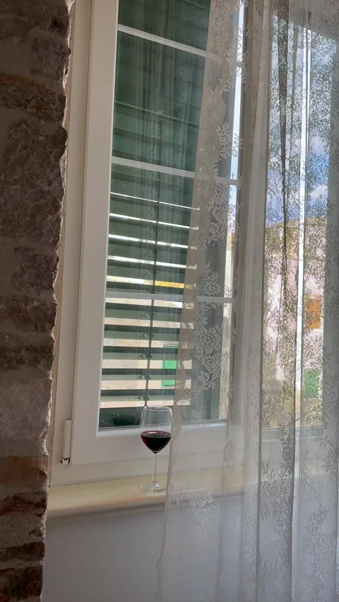 A glass of red wine on a windowsill with lace curtains and stone wall Stock Footage 341664088
