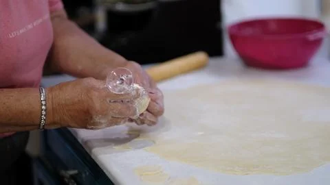 Glass rim cuts multiple round shapes from rolled dough as hands prepare pastry Stock Photos
