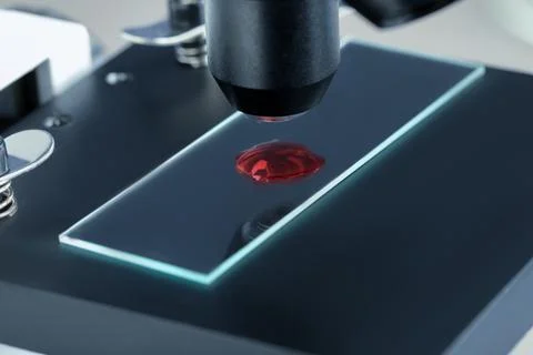 Glass slide with sample of red liquid under microscope in laboratory, closeup Stock Photos