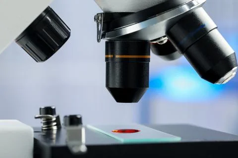 Glass slide with sample of red liquid under microscope in laboratory, closeup Stock Photos