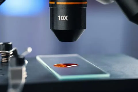 Glass slide with sample of red liquid under microscope in laboratory, closeup Stock Photos