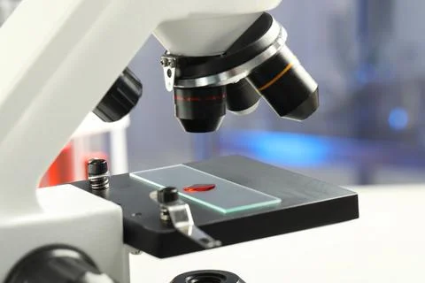 Glass slide with sample of red liquid under microscope in laboratory, closeup Stock Photos