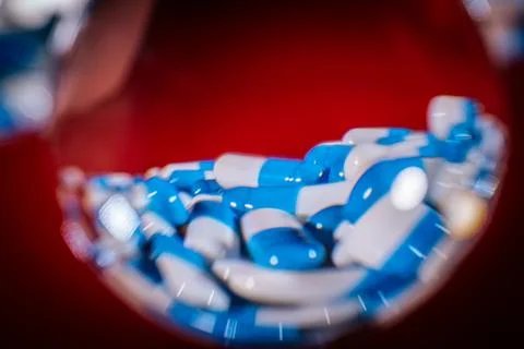 A glass sphere reflects a stack of blue and white capsules against. 스톡 사진