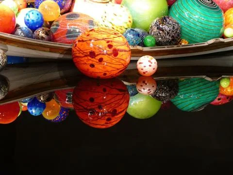 Glass spheres varying in size, pattern, nestled in boat-shaped vessel, refl.. Stock Photos