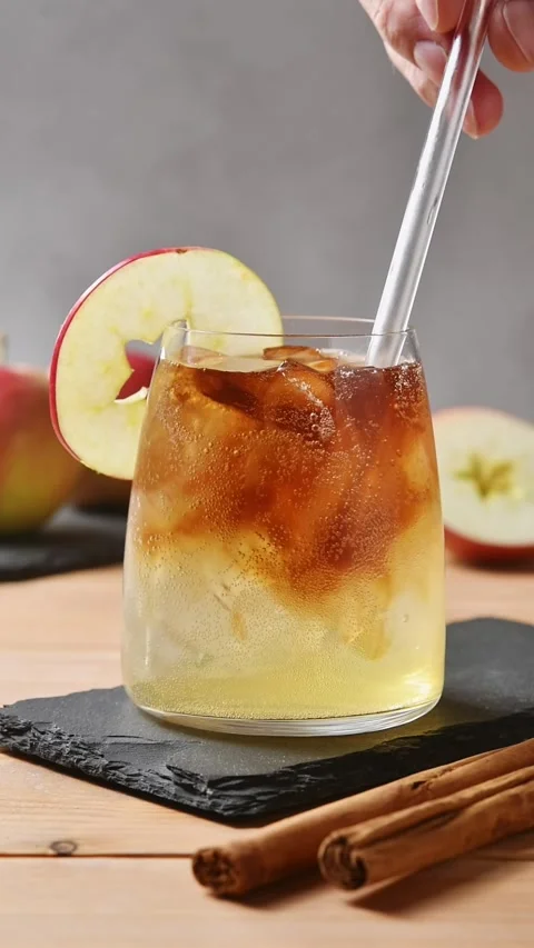 Glass straw stirs apple cider cold brew tonic, blending coffee layers with ice Stock Footage 345558278