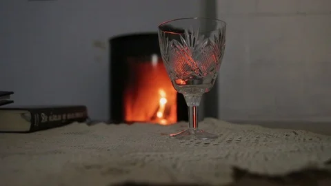 Glass on the table in the room there is a fireplace evening romanticism book Stock Footage 94384657