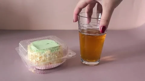 A glass of tea and a transparent plastic container with a pie with cream and Stock Footage 324698381