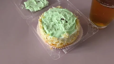 A glass of tea and a transparent plastic container with a pie with cream and Stock Footage 324698401