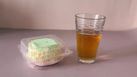 A glass of tea and a transparent plastic container with a pie with cream and Stock Footage 324698655